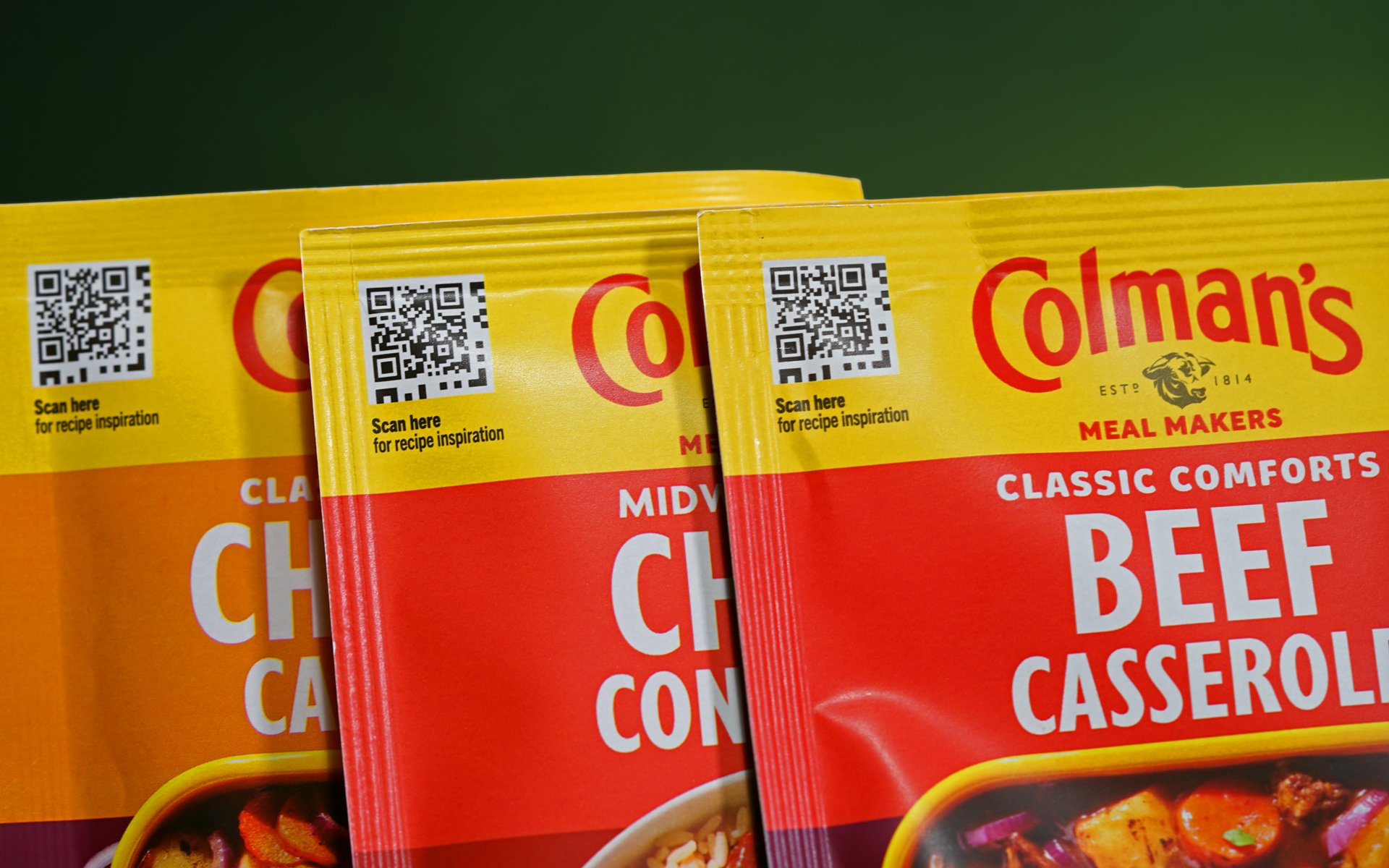 A close-up photograph of three Colman’s recipe mixes in sachets, all three of different flavours. In the top left corner of each packet, there is an accessible QR code, accompanied by a text below reading ‘Scan here for recipe inspiration’. The accessible QR codes are different for each flavour.