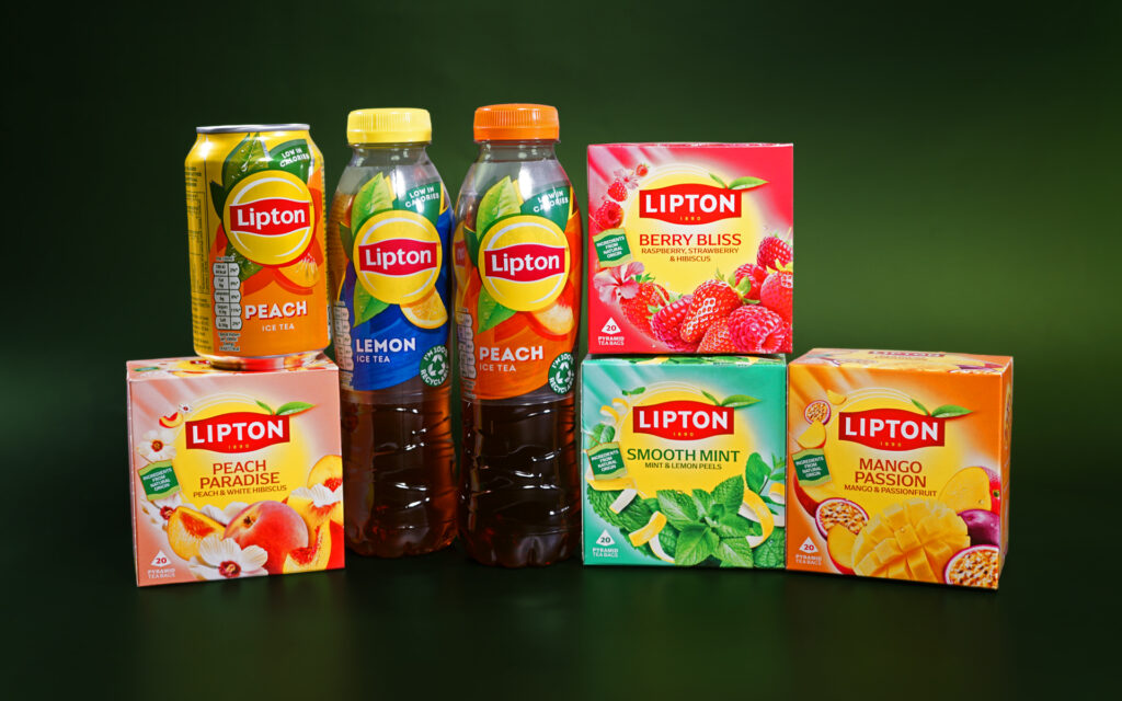 Various Lipton Teas and Infusions products are lined up next to each other against a dark green background. There are four boxes of tea bags, all of different flavours. On top of one of the boxes, there is a can of iced tea. In the middle, there are two bottles of iced tea.